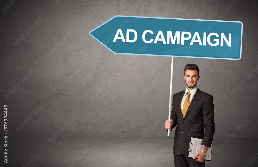 Young business person in casual holding road sign with AD CAMPAIGN inscription, new business direction concept Young business person in casual holding road sign with AD CAMPAIGN inscription, new business direction concept