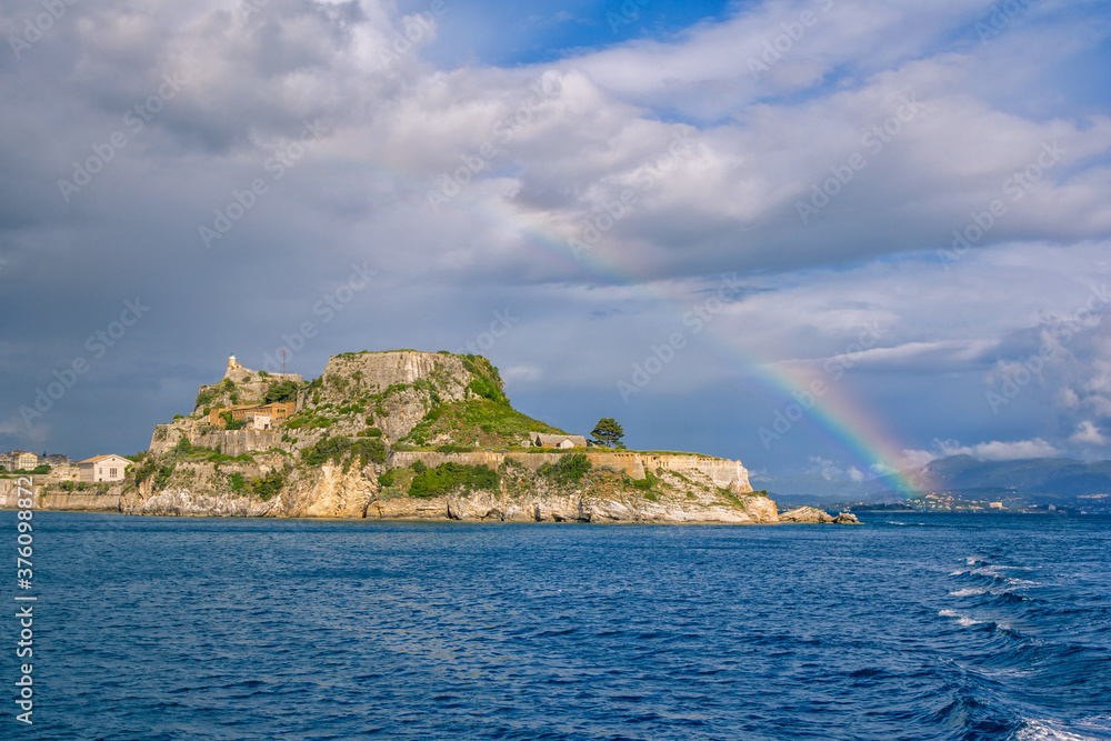 View of ancient venetian fortress on the hill at Corfu Island, Greece. Old stone walls, covered with green grass, sea bay, blue sky and rainbow View of ancient venetian fortress on the hill at Corfu Island, Greece. Old stone walls, covered with green grass, sea bay, blue sky and rainbow