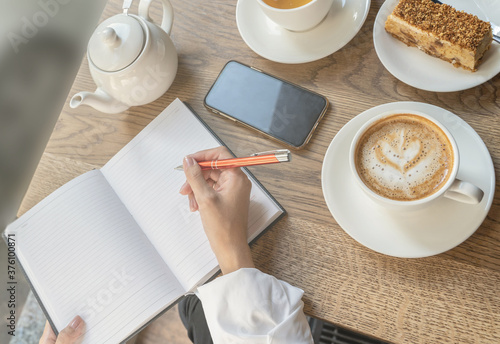 The girl writes notes in her diary with an orange pen over a Cup of tea.