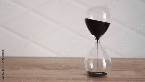 Crystal hourglass with black sand on wooden table and white background