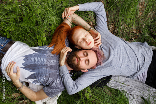 Top view of a couple, seated down on a green grass, seated down with turned heads with closed eyes. Couple relationship.