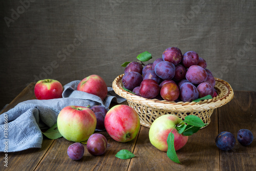Fresh harvest of red apples and plums in a wicker basket. Healthy tasty fruits.