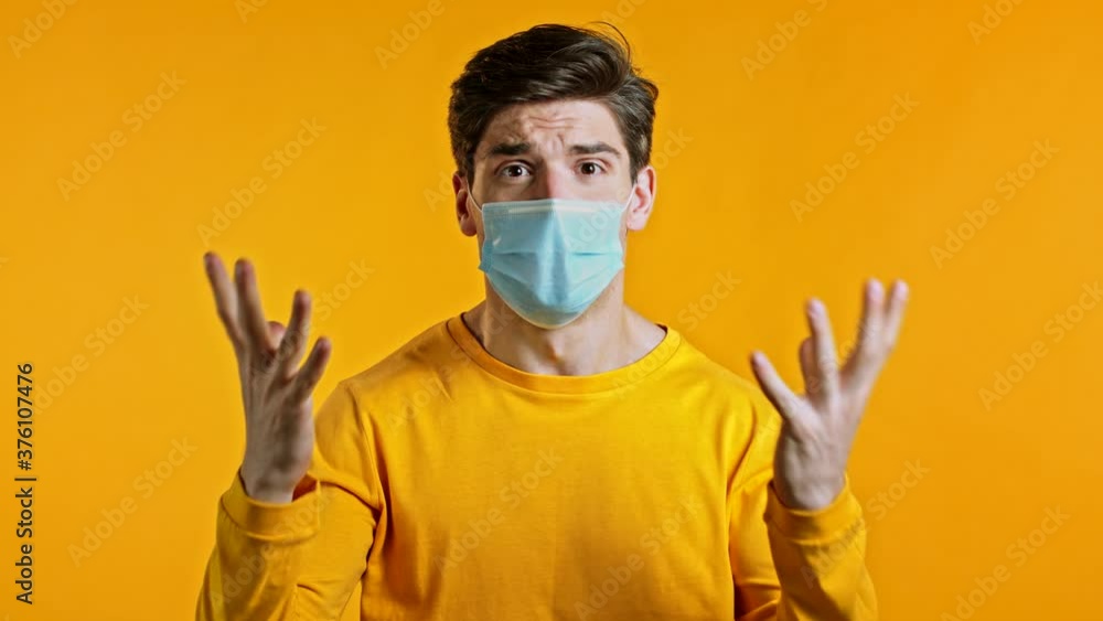 Angry irritated man in a protective mask screaming, asks when it will all end. Guy is tired of quarantine. Yellow studio background. Concept of pandemic, covid, corona virus Angry irritated man in a protective mask screaming, asks when it will all end. Guy is tired of quarantine. Yellow studio background. Concept of pandemic, covid, corona virus