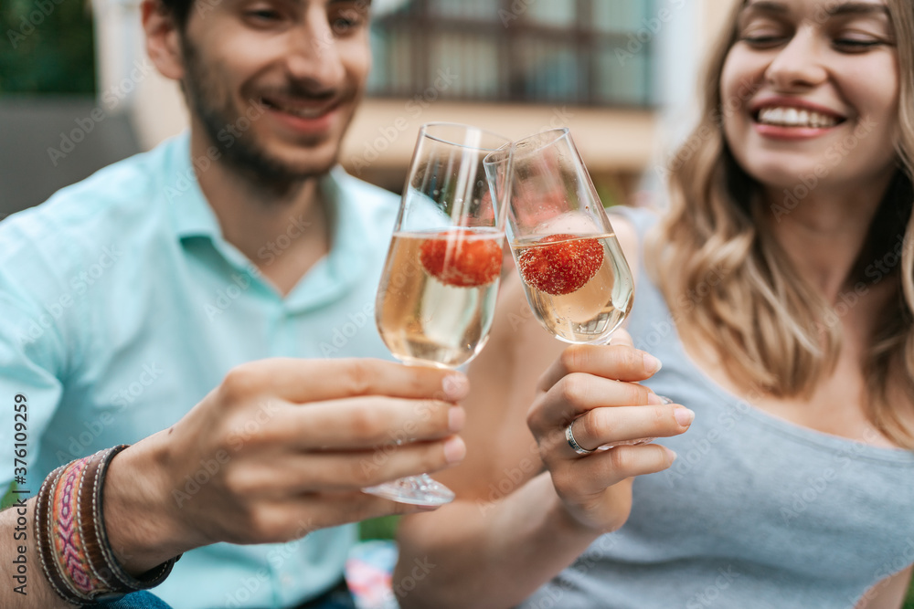Happy couple portrait clinking two glasses with sparkling wine and strawberries inside with blurred house on background. Celebrating love Happy couple portrait clinking two glasses with sparkling wine and strawberries inside with blurred house on background. Celebrating love
