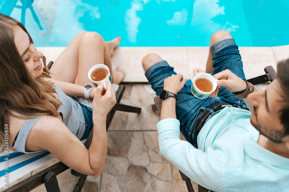 Lovely young couple spend time together at home near the pool while chatting and enjoying tea - obrazy, fototapety, plakaty 