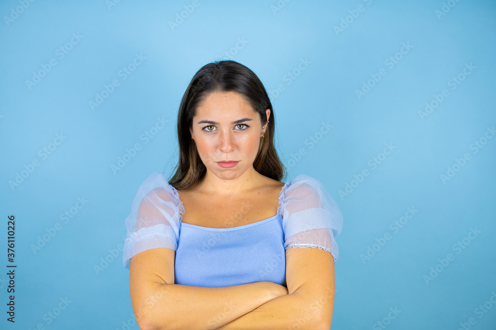 Young beautiful woman over isolated blue background skeptic and nervous, disapproving expression on face with crossed arms Young beautiful woman over isolated blue background skeptic and nervous, disapproving expression on face with crossed arms