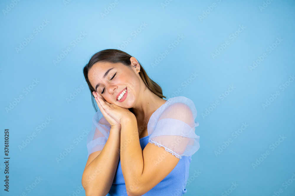 Young beautiful woman over isolated blue background sleeping tired dreaming and posing with hands together while smiling with closed eyes. Young beautiful woman over isolated blue background sleeping tired dreaming and posing with hands together while smiling with closed eyes.