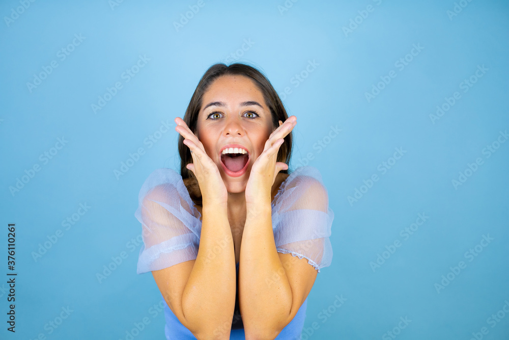 Fototapeta premium Young beautiful woman over isolated blue background screaming and surprised with her hands around her mouth