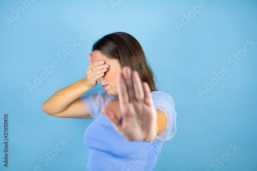 Young beautiful woman over isolated blue background covering eyes with hands and doing stop gesture with sad and fear expression. Embarrassed and negative concept.