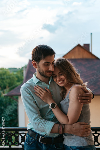 Man embracing wife at balcony. Relaxed couple enjoy day and good news. Happy young family