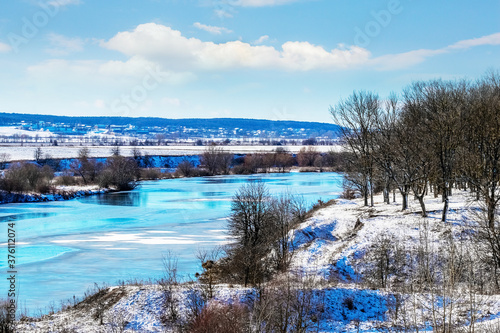 Winter landscape with trees on a hill by the river