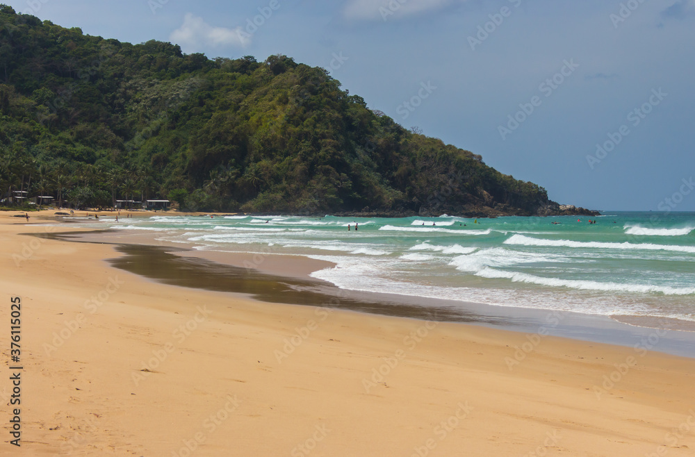 Tropical beach on sunny day with surfers. Duli surf beach in Palawan, Philippines. Wide beach with green mountain on background. Tropical landscape. Azure water in idyllic lagoon. Paradise nature. 
