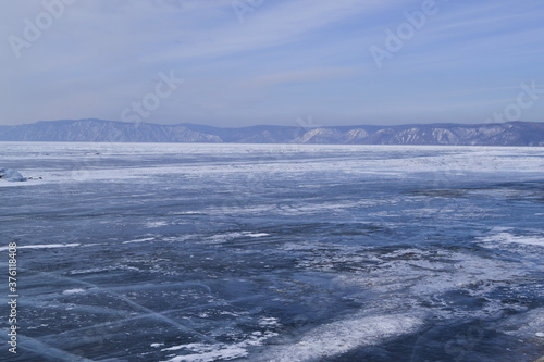 large iridescent crystals white blue ice with cracks glow in the light of the sun  lake baikal in winter  mountains on the horizon