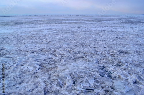 iridescent crystals white blue ice floes with cracks glow in the light of the sun, lake baikal in winter, mountains on the horizon