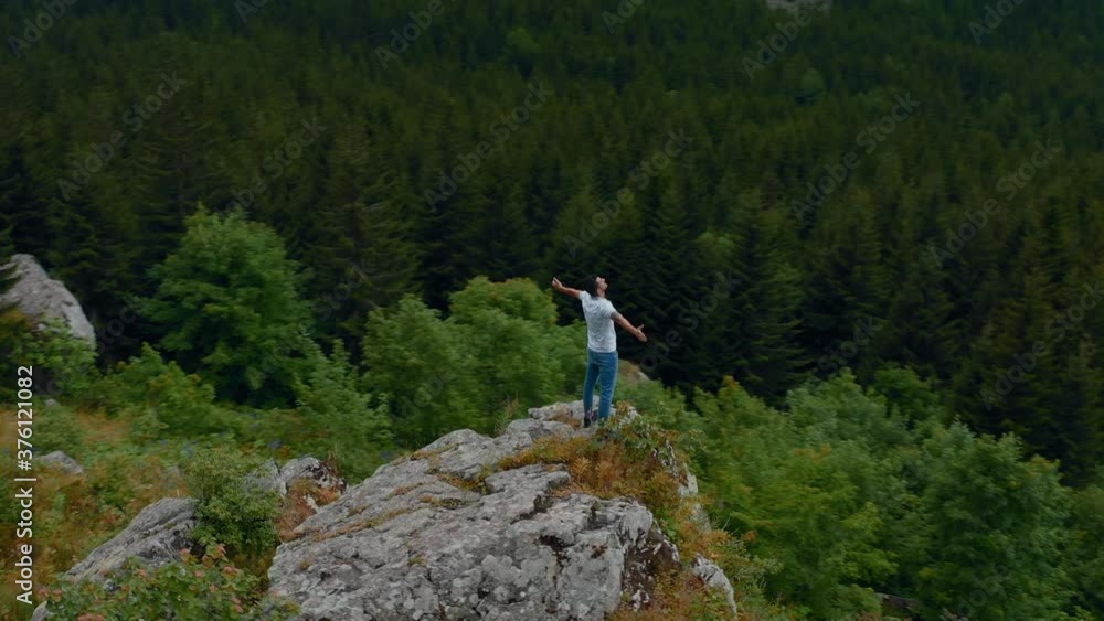 Drone Fly. On the rock, young adult with open arms watches the pine trees. Freedom concept 4k