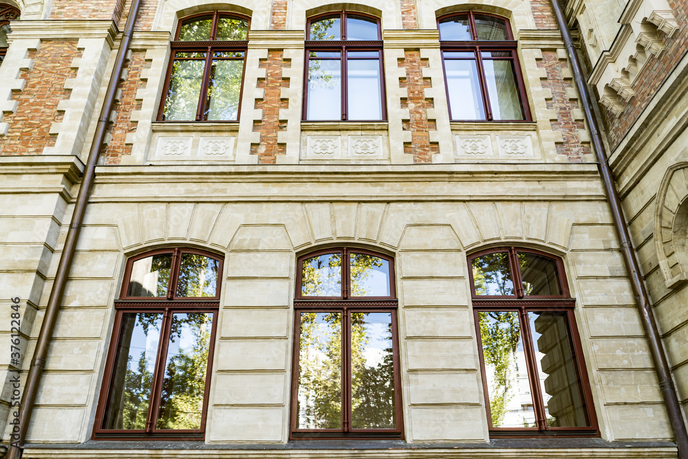 Obraz premium Down angle of arched windows on old beautiful building with sky and trees reflection in the glass