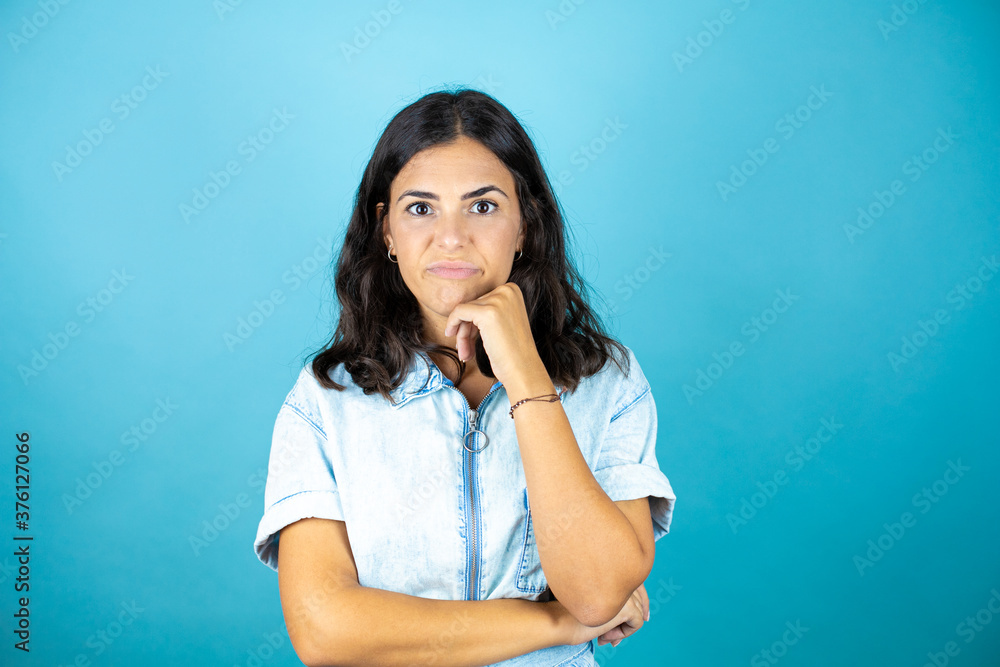 Young beautiful woman wearing a denim jumpsuit over isolated blue background Young beautiful woman wearing a denim jumpsuit over isolated blue background