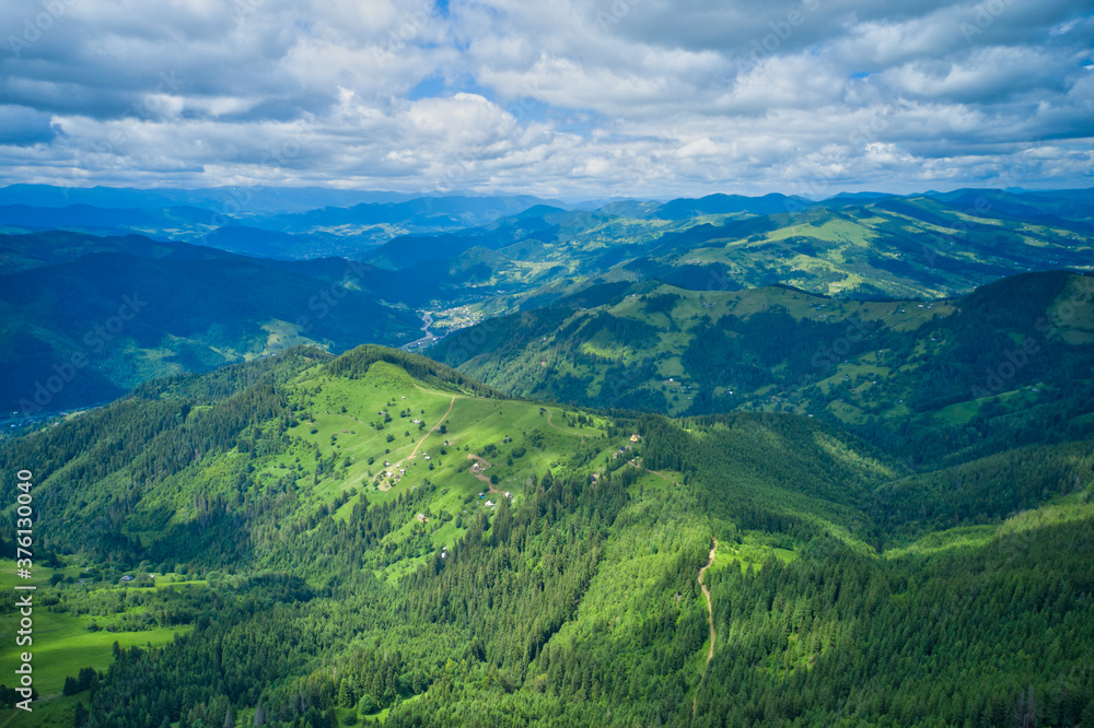 Aerial drone view of houses in the green forested mountains.