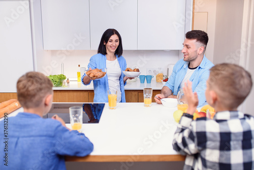 Joyful family of four persons drink orange juice with croissants and tasty cakes in the kitchen. Happy family concept.
