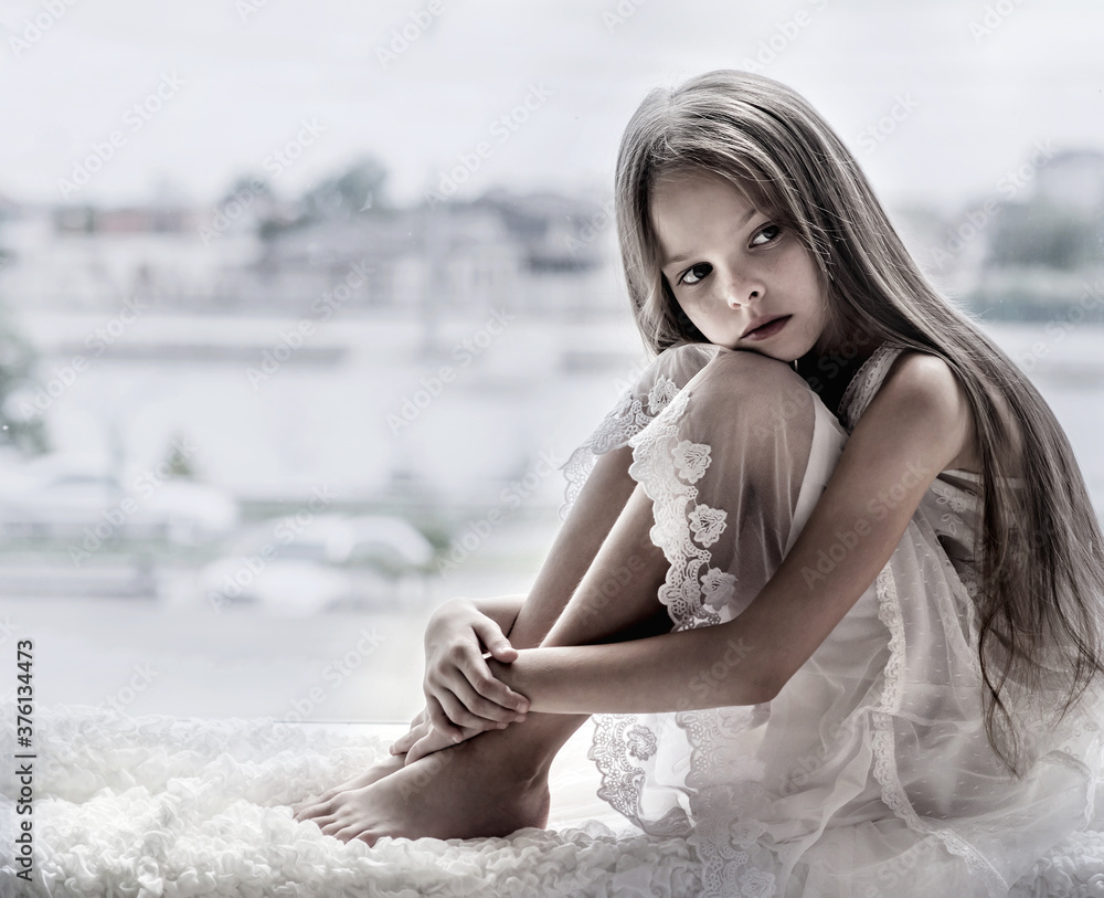 Sad little girl sits alone front of the window. Sad little girl sits alone front of the window.