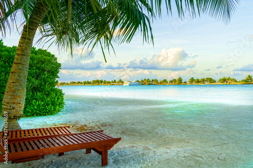 Fototapeta Naklejka Na Ścianę i Meble -  Sandy Beach with Wooden Deck Chairs Shaded by Palm Tree