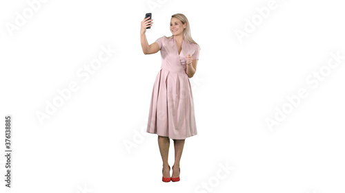 Mature woman wearing light pink dress making selfie on white background.