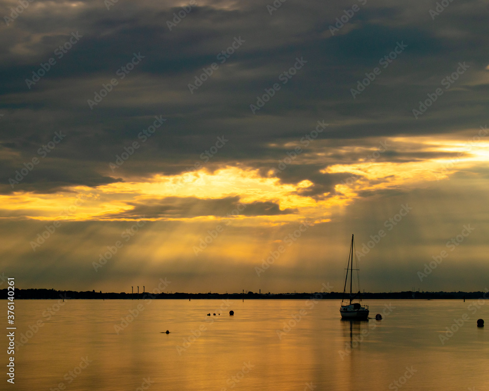 Light rays through the clouds at sunset shining down on a single yacht or sailing boat 