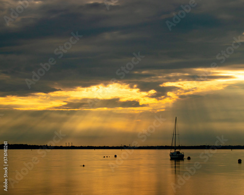 Light rays through the clouds at sunset shining down on a single yacht or sailing boat  © Gary L Hider