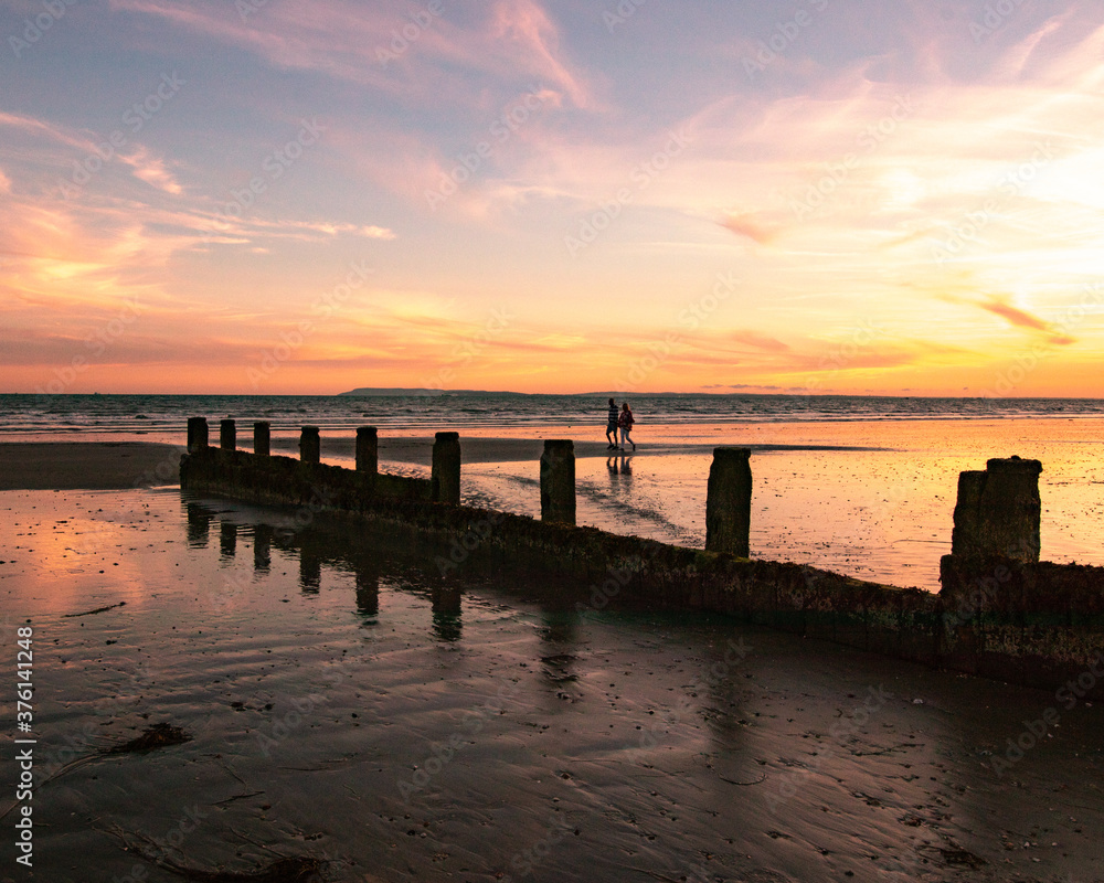 Fototapeta premium A couple walking along a sandy beach at sunset 
