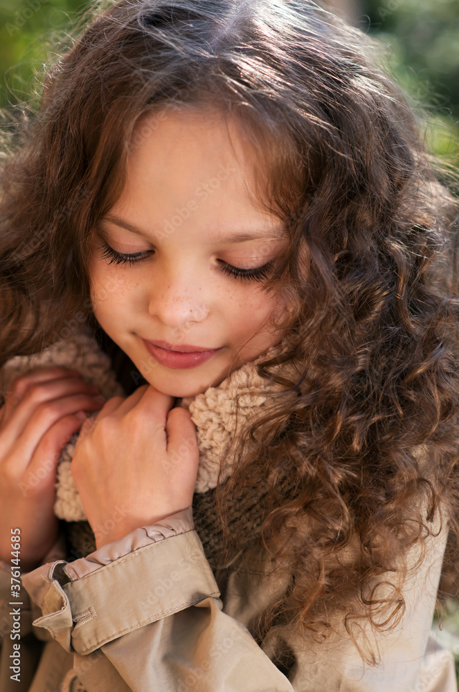 Portrait of little cute smiling girl with long curly hair in stylish retro coat walking in the garden or park. Portrait of little cute smiling girl with long curly hair in stylish retro coat walking in the garden or park.
