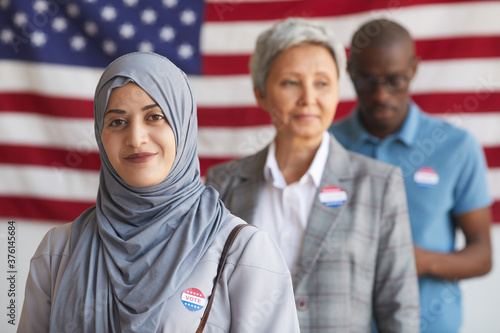 Multi-ethnic group of people at polling station on election day, focus on smiling Arab woman with I VOTED sticker looking at camera, copy space photo