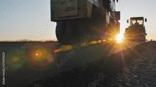 Two road rollers line the asphalt at sunset. Road surface repair. Construction of a new road. Road construction machines. A layer of freshly laid asphalt.