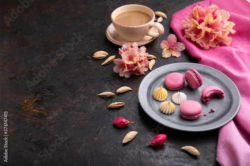 Purple macarons or macaroons cakes with cup of coffee on a black concrete background. Side view, copy space.