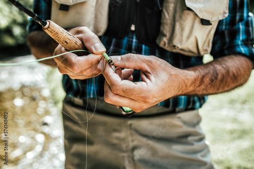 Close up shot of senior fisherman s hands tying a fly for fishing. Fly fishing concept.