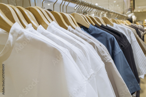 White, khaki, blue, black tone fabric shirts hanging on a rack in a store.