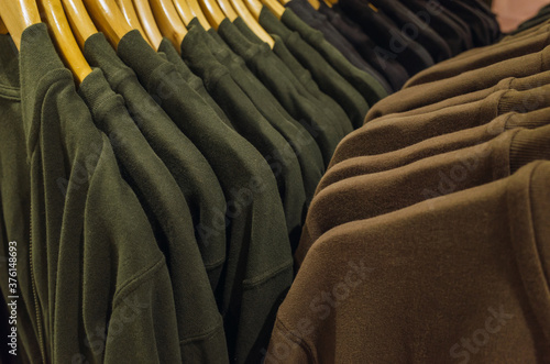 Green and brown tone fabric shirts hanging on a rack in a store.