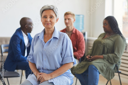 Portrait of smiling mature woman looking at camera during support group meeting with people sitting in circle  copy space