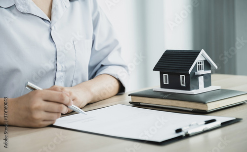 Model home standing in front of Real estate agent hand holding a pen, point to business contract, rent, buy, mortgage, loan, home insurance