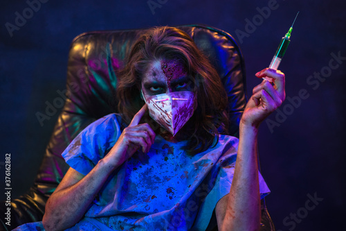 Halloween zombie with coronavirus Woman wearing face mask Kn95 protective for Covid-19 holding a syringe with antidote . Horror infection concept photo