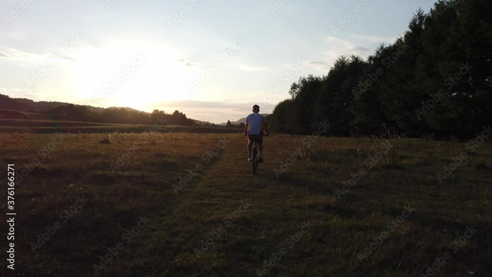 Male rides a bicycle in the sunset light along the village road. Boy riding his bike on a summer day. Male rides a bicycle in the sunset light along the village road. Boy riding his bike on a summer day.