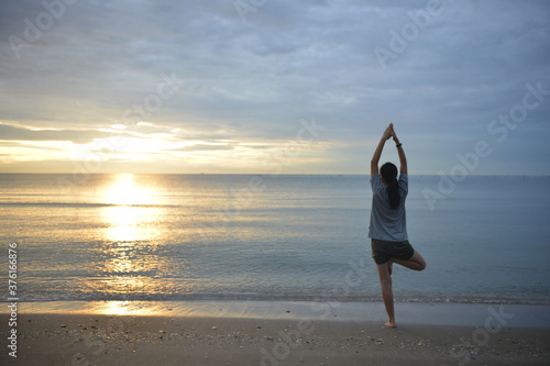 Healthy woman doing Yoga exercises on the beach at sunrise time