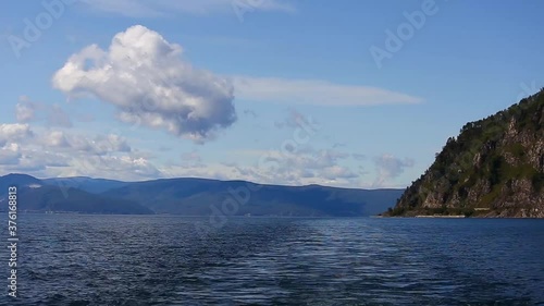 Water behind big motor boat at Baikal lake with rocky shore a far and blue sky with clouds