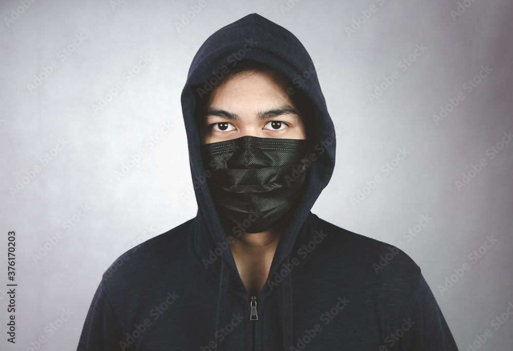 An image of a man in a hood or a jig on a dark gray background with a black mask covering his mouth and nose. An image of a man in a hood or a jig on a dark gray background with a black mask covering his mouth and nose.
