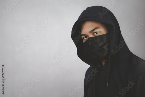 An image of a man in a hood or a jig on a dark gray background with a black mask covering his mouth and nose.