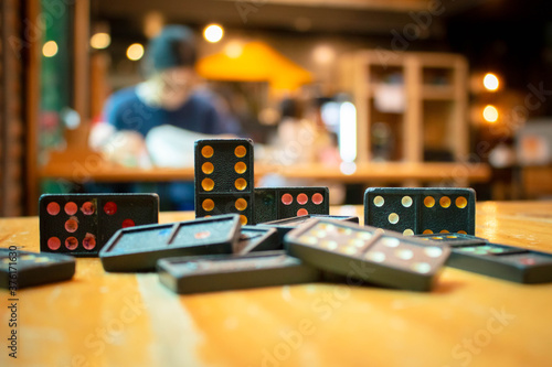 Close up old black color dominoes with colorful dot pieces. Falling Black Dominos on wooden desk with bokeh background.