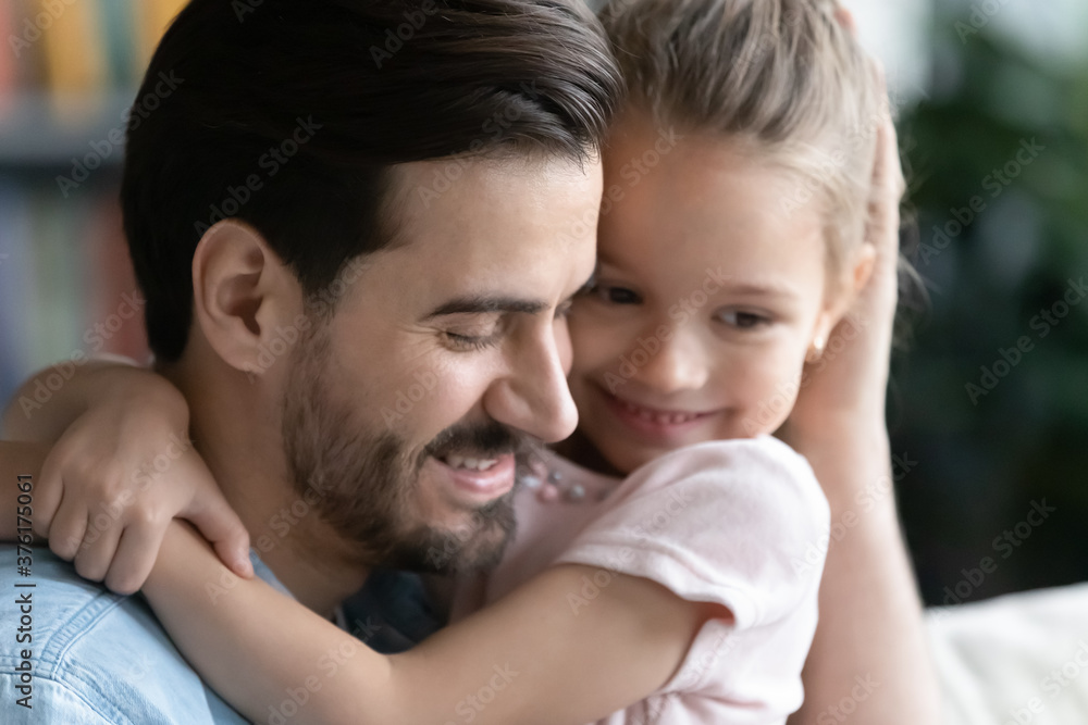 Close up loving young father hugging pretty little daughter, sitting on cozy couch at home, caring dad and preschool girl cuddling enjoying tender moment, good family relationship concept Close up loving young father hugging pretty little daughter, sitting on cozy couch at home, caring dad and preschool girl cuddling enjoying tender moment, good family relationship concept