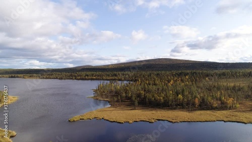 Aerial view behind trees, revealing a lake, wetlands, fell mountains and autumn color foliage forest, sunny, autumn day, in Norbotten, Lappland, Sweden - Rising, drone shot photo