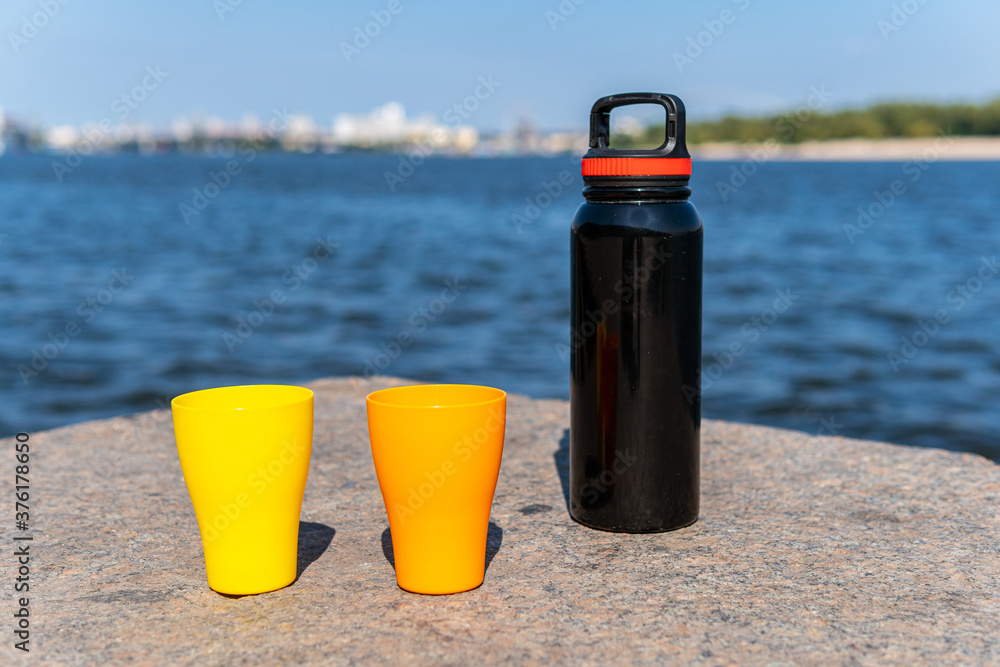 Two plastic caps (yellow and orange) and a thermos on a concrete barrier wall near a blue sea Two plastic caps (yellow and orange) and a thermos on a concrete barrier wall near a blue sea