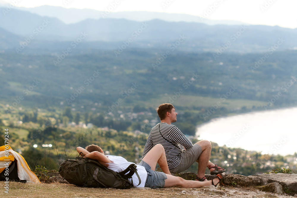 Pair of tourists - man and woman having rest in the picturesque place with sea and mountain view. Copy space