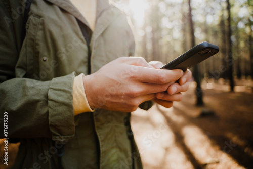 Young caucasian male texting on smartphone while standing in earthy forest.